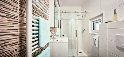 Baño moderno en Panorama Chalets con ducha acristalada, azulejos blancos y toallas en un radiador.