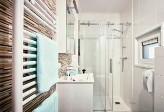 Baño moderno en Panorama Chalets con ducha acristalada, azulejos blancos y toallas en un radiador.