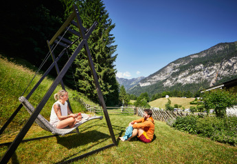 Due persone si rilassano ai Panorama Chalets, godendosi la vista panoramica di montagne e prati verdi.