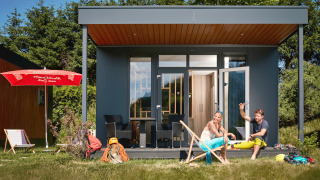 Twee mensen ontspannen voor een tiny house genaamd Studio met buitenstoelen en avonturenuitrusting.