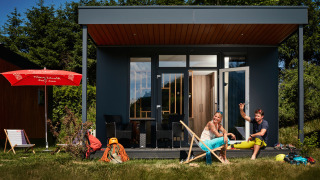 Dos personas se relajan frente a una tiny house llamada Studio, con sillas y equipo de aventura en el césped.