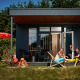 To personer slapper af foran et tiny house kaldet Studio med udendørs møbler og udstyr til eventyr.