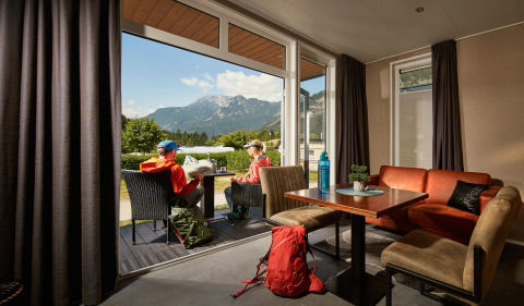 Twee personen zitten buiten bij een tiny house Studio op Camping Seeblick Toni in Oostenrijk met bergzicht.