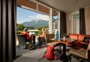 Due persone sedute fuori da una tiny house Studio al Camping Seeblick Toni in Austria con vista sulle montagne.