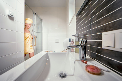 Vrouw komt onder de douche vandaan in Studio-badkamer op Camping Seeblick Toni, Oostenrijk, met handdoek.
