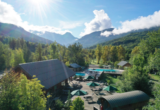 Billede af sommerhusområde med swimmingpool og bjerge i baggrunden ved Huttopia Vallouise, Provence-Alpes, Frankrig.