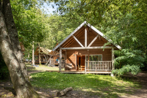 Wooden cabin surrounded by trees at Huttopia Versailles holiday park in Île de France, France, summer day.