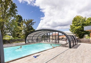 Outdoor swimming pool with glass cover and relaxing guests at Huttopia Versailles holiday park, Île de France.
