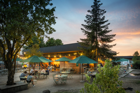 Outdoor dining area with green umbrellas and people at Huttopia Versailles holiday park at sunset.