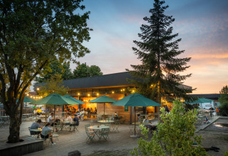 Outdoor dining area with green umbrellas and people at Huttopia Versailles holiday park at sunset.