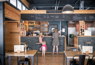 A woman with two children ordering food at the bar in a modern wood-paneled cafe at Huttopia Versailles, France.