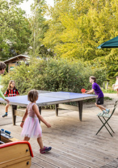 Kinder und Erwachsene spielen Tischtennis in einem Ferienpark in Île de France, umgeben von Bäumen.