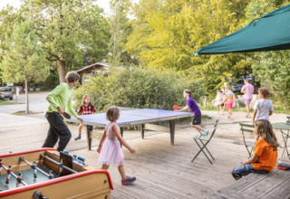 Kinderen en volwassenen spelen tafeltennis buiten in een vakantiepark in Île de France, omgeven door natuur.