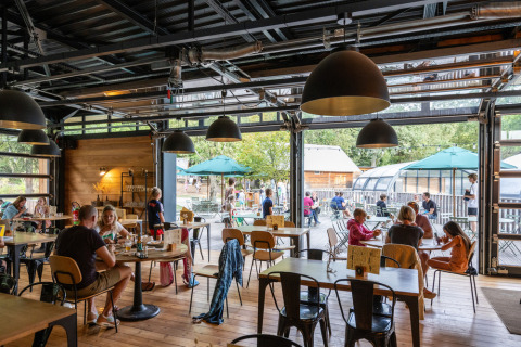 Huéspedes disfrutan comidas dentro y fuera en el restaurante de Huttopia Versailles en Île-de-France, Francia.