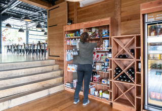 Persona organizando productos en una estantería de madera en una tienda, con botellas de vino y bebidas cerca.