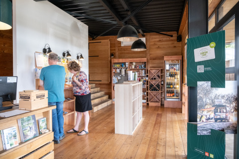 Dos personas exploran la zona de información en la tienda de recepción de Huttopia Versailles, Île de France.