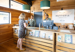 Reception area of Huttopia Versailles holiday park in Île de France, France, with staff and guest.