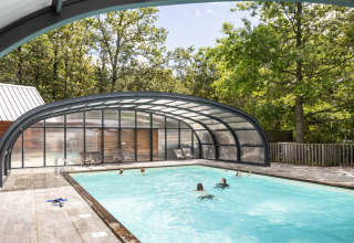 Udendørs swimmingpool med delvist overdækning og gæster, omgivet af træer, ved Huttopia Versailles i Frankrig.