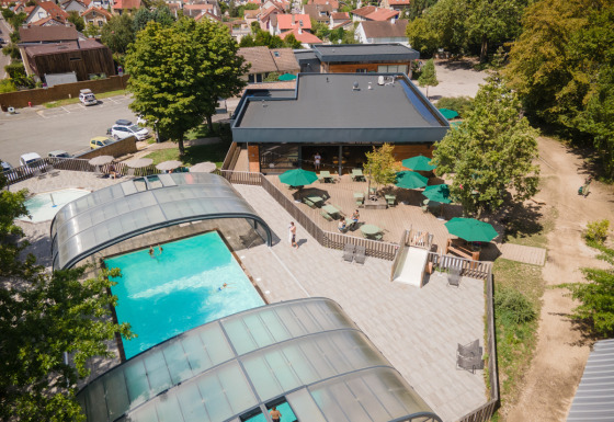 Luchtfoto van Huttopia Versailles vakantiepark met overdekt zwembad, zonneterras en buitenzitjes.