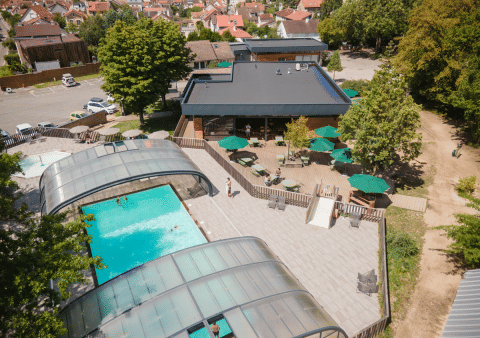 Luftfoto af Huttopia Versailles feriepark med overdækket swimmingpool, solterrasse og udendørs siddepladser.