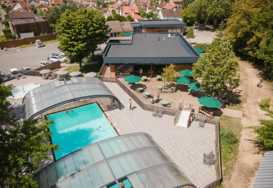 Luftfoto af Huttopia Versailles feriepark med overdækket swimmingpool, solterrasse og udendørs siddepladser.
