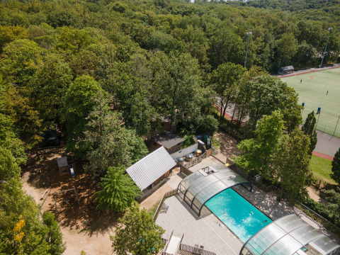 Vista aérea del parque vacacional Huttopia Versailles con piscina cubierta, bosque y canchas en Île de France.