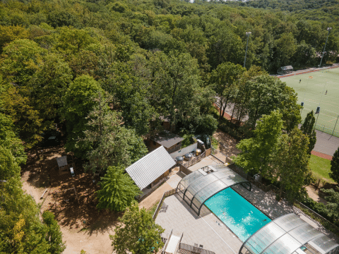 Vue aérienne du parc de vacances Huttopia Versailles avec piscine couverte, forêt et terrains de sport en Île de France.