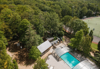 Vista aerea di Huttopia Versailles con piscina coperta, area boschiva e campi sportivi in Île de France, Francia.