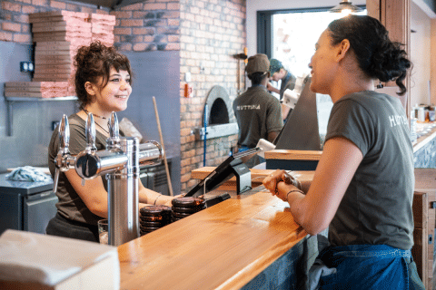 Two staff members chatting happily at the counter in Huttopia Versailles holiday park, Île de France.