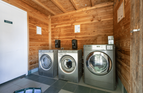 Laundry room at Huttopia Versailles featuring three modern washing machines and wooden walls in Île de France.