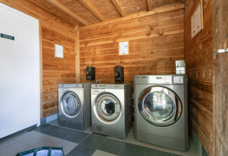 Laundry room at Huttopia Versailles featuring three modern washing machines and wooden walls in Île de France.