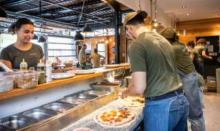 Staff prepare fresh pizzas in the open kitchen at Huttopia Versailles holiday park in Île de France.