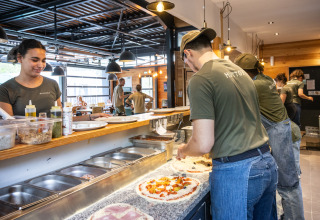 Het personeel maakt verse pizza’s in de open keuken van Huttopia Versailles in Île de France.