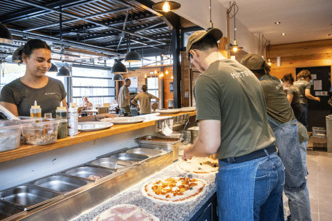 Lo staff prepara pizze fresche nella cucina a vista dell'Huttopia Versailles a Île de France.