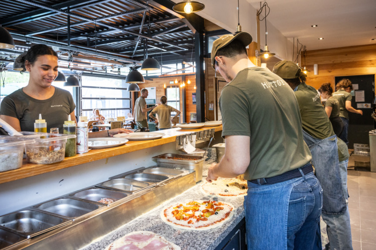 Mitarbeiter bereiten frische Pizza in der offenen Küche im Ferienpark Huttopia Versailles zu.