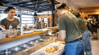 El equipo prepara pizzas frescas en la cocina abierta de Huttopia Versailles en Île de France.