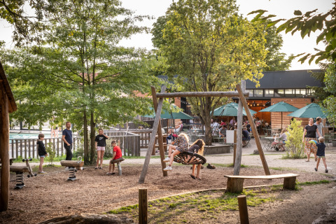 Niños juegan en un columpio mientras adultos descansan cerca en Huttopia Versailles, Île de France, Francia.