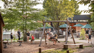 Niños juegan en un columpio mientras adultos descansan cerca en Huttopia Versailles, Île de France, Francia.
