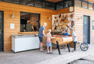 Children and an adult play foosball outside a wooden building at Huttopia Versailles holiday park, Île-de-France.