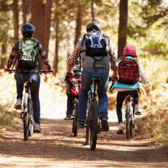 Familie fährt gemeinsam Fahrrad durch den Wald im Huttopia Versailles Feriendorf in Île de France, Frankreich.