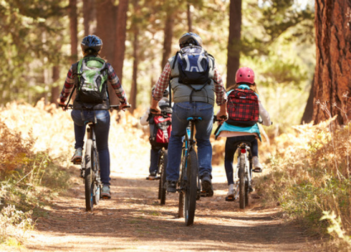 Famille faisant du vélo sur un sentier forestier à Huttopia Versailles, Île de France, France.