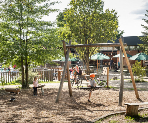 Niños juegan en el parque infantil de Huttopia Versailles, rodeado de árboles en Île de France, Francia.