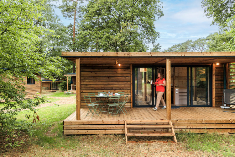 Wooden cabin with a terrace and garden table at Huttopia De Meinweg holiday park, Limburg, Netherlands, in nature.