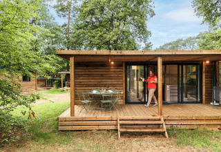 Wooden cabin with a terrace and garden table at Huttopia De Meinweg holiday park, Limburg, Netherlands, in nature.