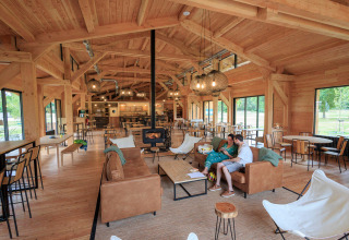 Gezellige, ruime lounge met houten interieur en grote ramen bij Huttopia De Meinweg in Limburg, Nederland.