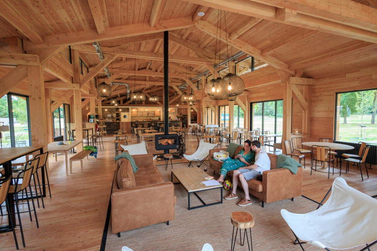 Spacious wooden lodge with modern seating, large windows, and a cozy atmosphere at Huttopia De Meinweg, Limburg.