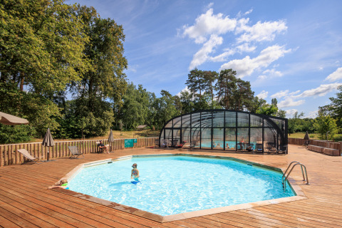 Piscina al aire libre con terraza de madera y sombrillas en Huttopia De Meinweg en Limburgo, Países Bajos.