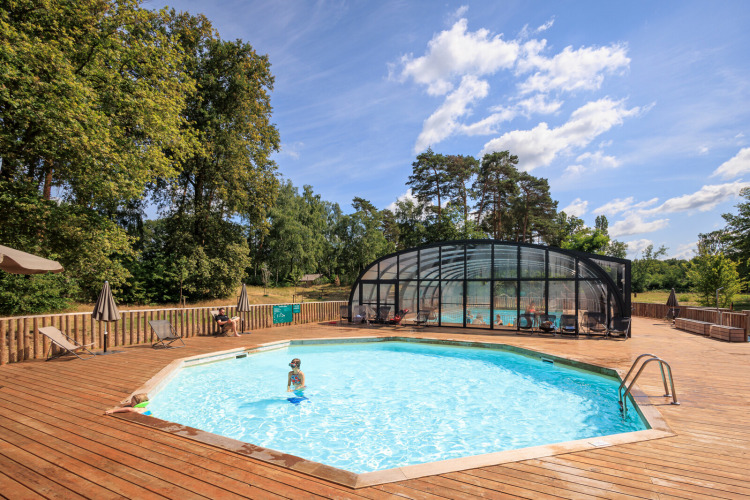 Outdoor swimming pool with wooden deck and umbrellas at Huttopia De Meinweg holiday park in Limburg, Netherlands.
