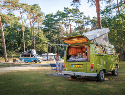 Familie nyder camping ved en grøn campervan under træer i Huttopia De Meinweg, Limburg, Nederlandene.