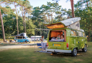 Famiglia si rilassa vicino a un camper verde nel parco vacanze Huttopia De Meinweg, Limburgo, Paesi Bassi.